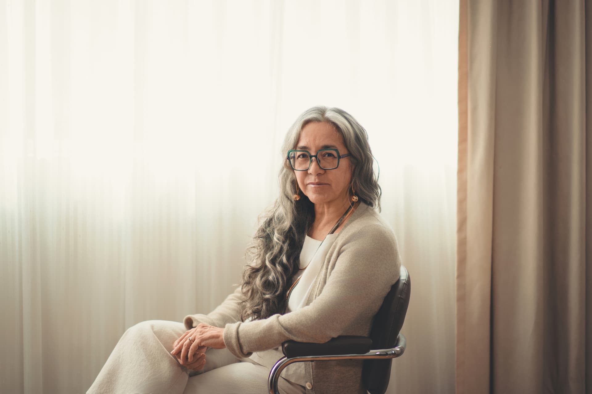 Retrato original de Cristina Rivera Garza sentada junto a una cortina